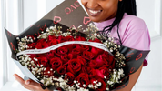 Smiling woman holding large red rose bouquet with baby’s breath, beautifully wrapped for a romantic surprise