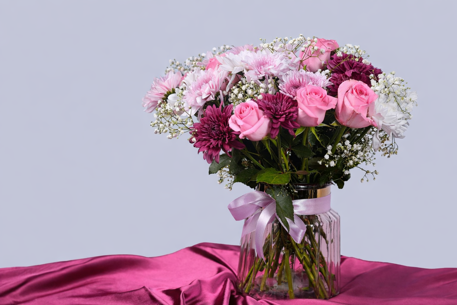 Pink rose and chrysanthemum bouquet with baby’s breath in a glass vase tied with a ribbon, styled for elegant gifting