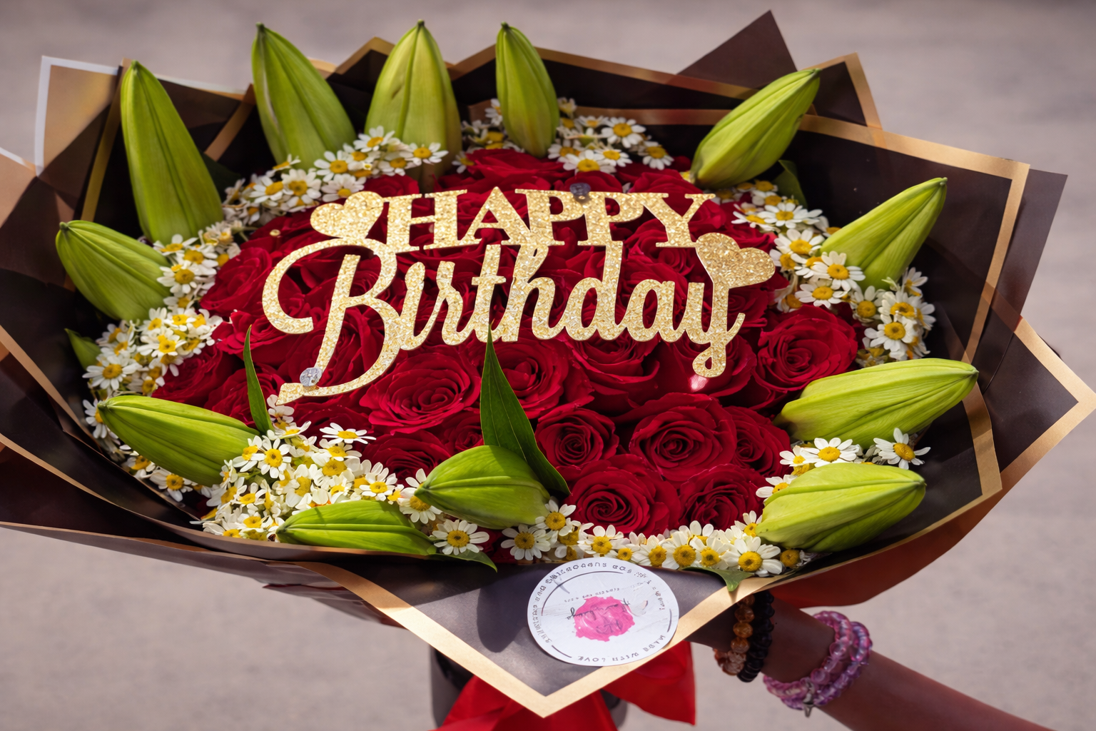 Red rose birthday bouquet with white daisies and green lily buds, featuring a gold “Happy Birthday” topper and elegant wrapping.