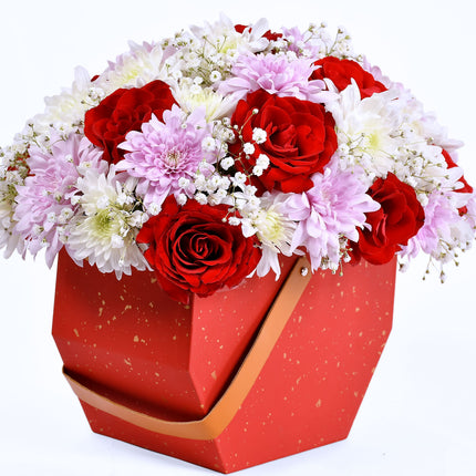 Enchant box flower arrangement with red roses, pink chrysanthemums, and baby’s breath in red gift box.