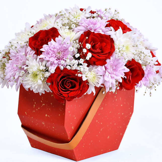 Enchant box flower arrangement with red roses, pink chrysanthemums, and baby’s breath in red gift box.