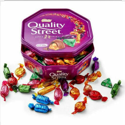 Quality Street assorted chocolates tin with colourful wrapped sweets scattered around on white background