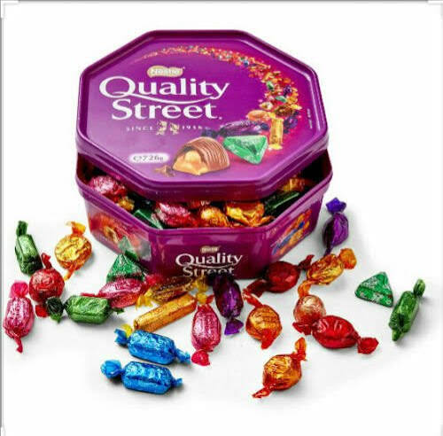 Quality Street assorted chocolates tin with colourful wrapped sweets scattered around on white background