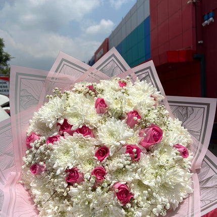 Large bouquet of white chrysanthemums and pink roses with baby’s breath in decorative wrap outdoors near building