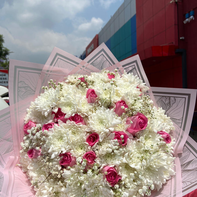 Large bouquet of white chrysanthemums and pink roses with baby’s breath in decorative wrap outdoors near building