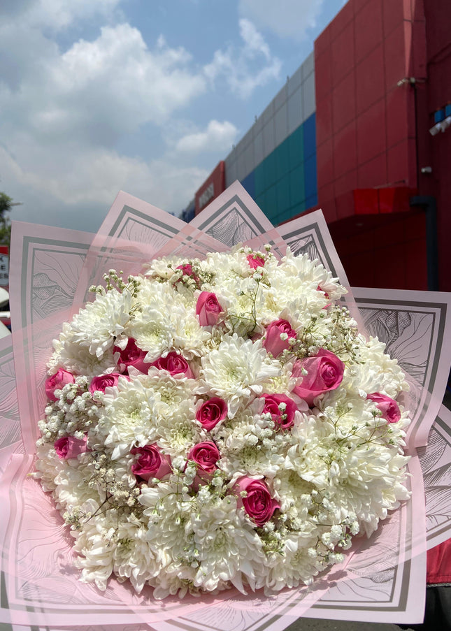 Large bouquet of white chrysanthemums and pink roses with baby’s breath in decorative wrap outdoors near building