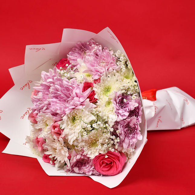 Treasure bouquet with pink roses, white and pink chrysanthemums, and baby’s breath in white wrap.