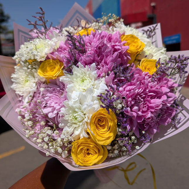 Pop of colour bouquet with pink and white chrysanthemums, yellow roses, and filler flowers in wrap.