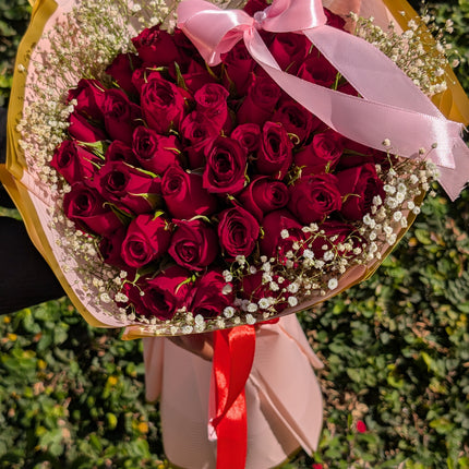 True Love Bouquet Pink with red roses, baby’s breath, and pink wrap tied with ribbon.