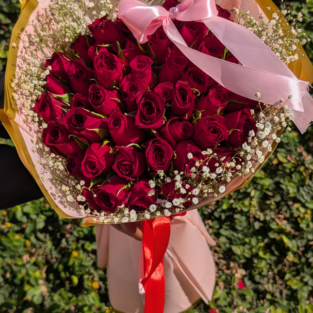 True Love Bouquet Pink with red roses, baby’s breath, and pink wrap tied with ribbon.